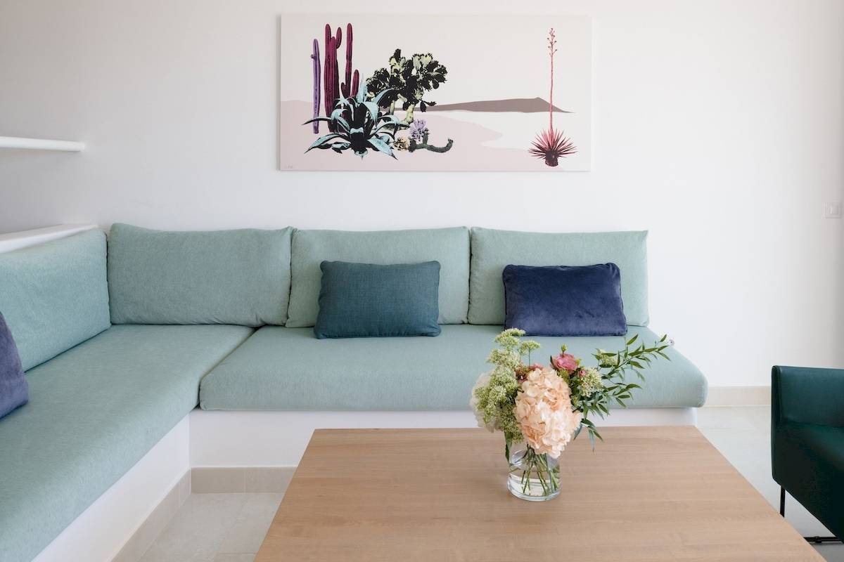 Wohnzimmer im Plus Fariones Suite Hotel mit grüner Couch, Blumenvase und Kunstwerk an der Wand.