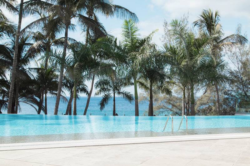 Ein Swimmingpool des Fariones Hotel mit Blick auf das Meer und Palmen im Hintergrund.