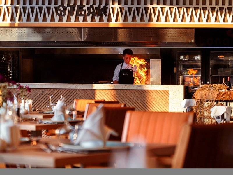 Koch in Steak-Restaurant beim Braten von Steaks mit Feuereffekt in der Küche.