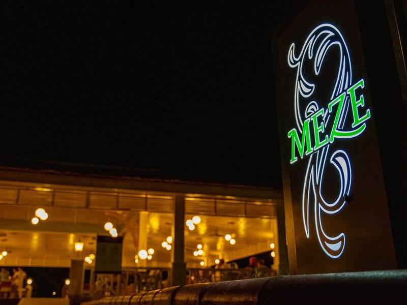Nachtansicht des Ducale Lara Hotels mit leuchtendem Neon-Schild 'Meze'.