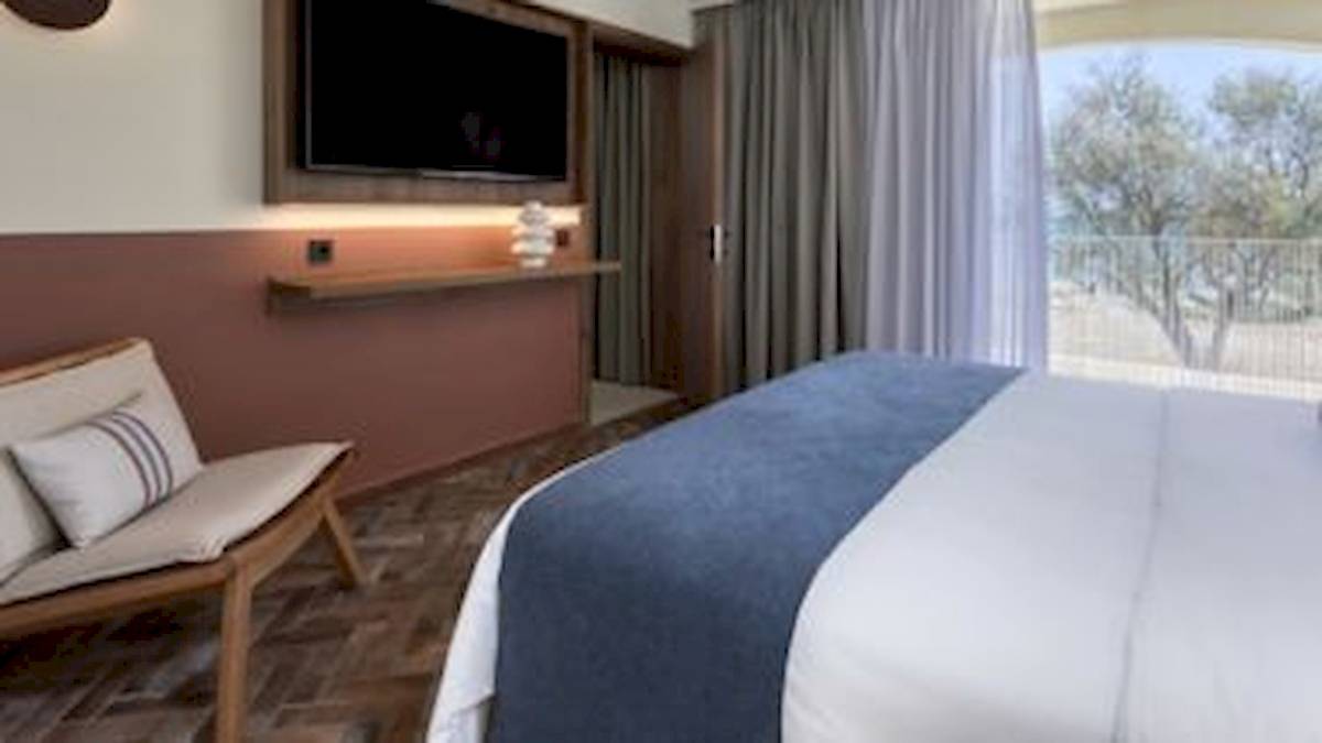 Hotelzimmer im Domes Aulus Zante mit Bett, Fernseher und Blick auf Bäume.