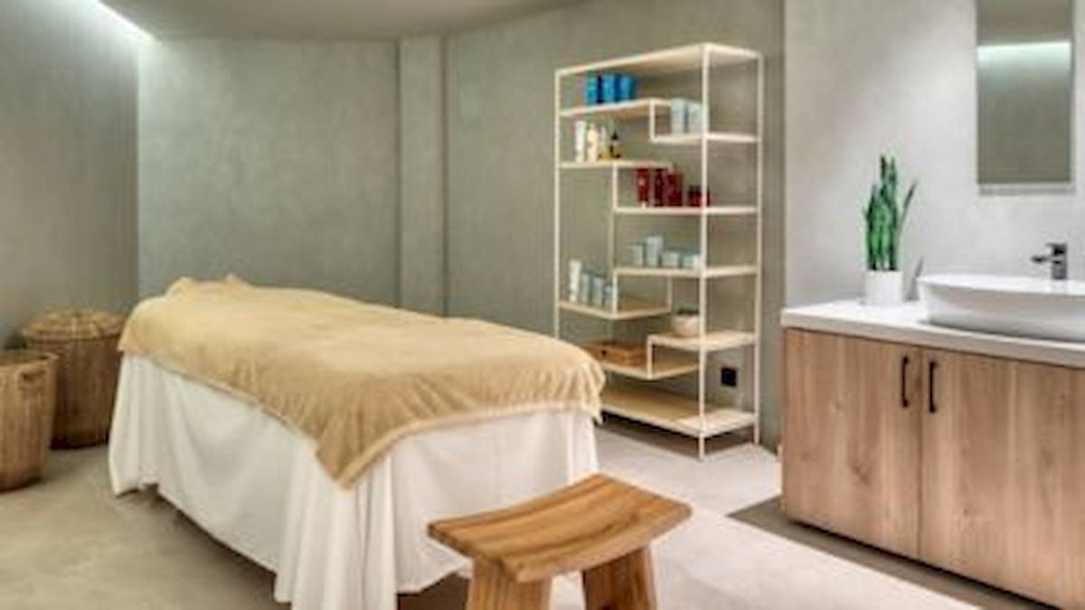 Massageraum im Domes Aulus Zante Hotel mit Massageliege, Regal, Waschbecken und Pflanze.