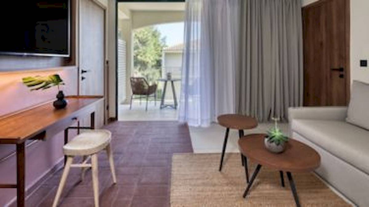 Innenansicht eines Zimmers im Domes Aulus Zante Hotel mit Wohnzimmer, Fernseher, Tisch und Stühlen.