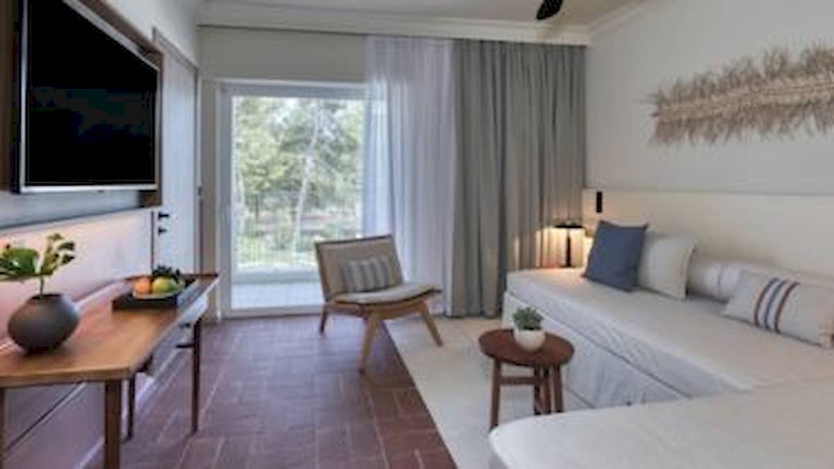 Innenansicht der Suite im Domes Aulus Zante Hotel mit Fernseher, Sofa, Tisch und Fenster.