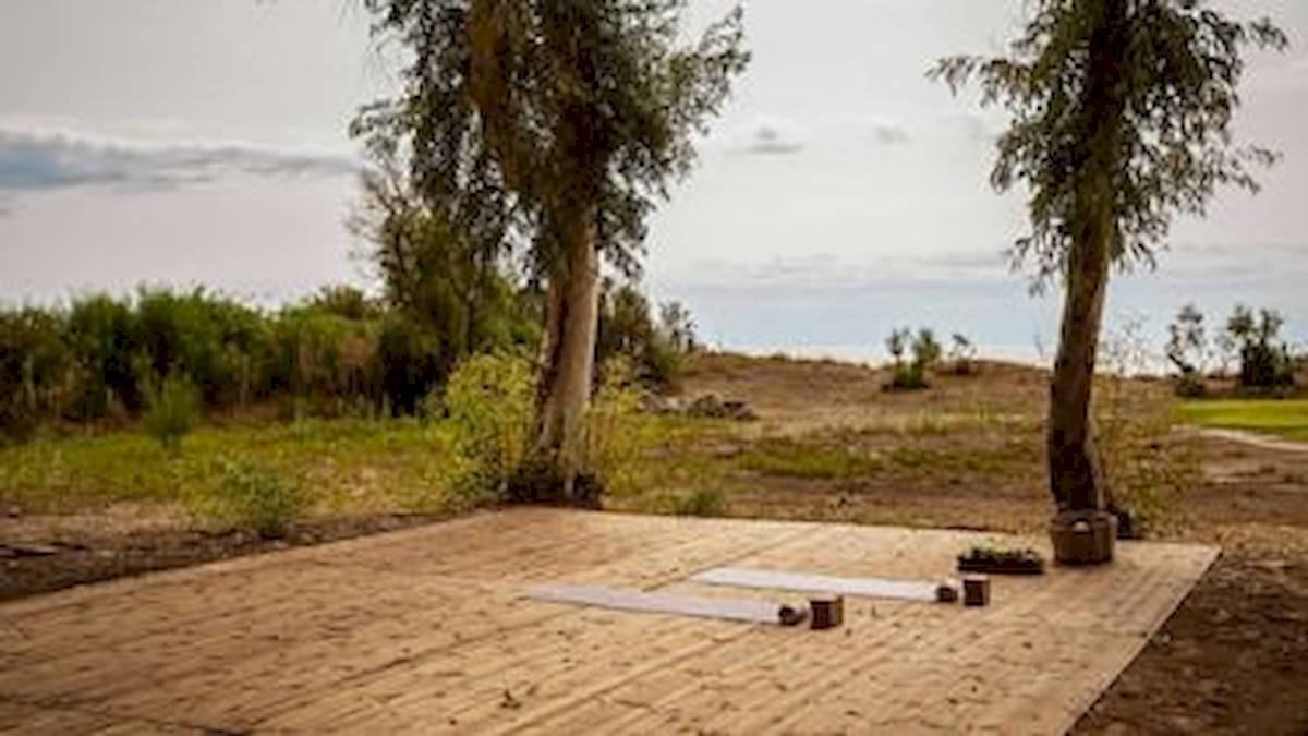 Yoga-Platz vor Bäumen im Freien mit zwei Matten, zwei Kerzen und einem Topf auf dem Boden.