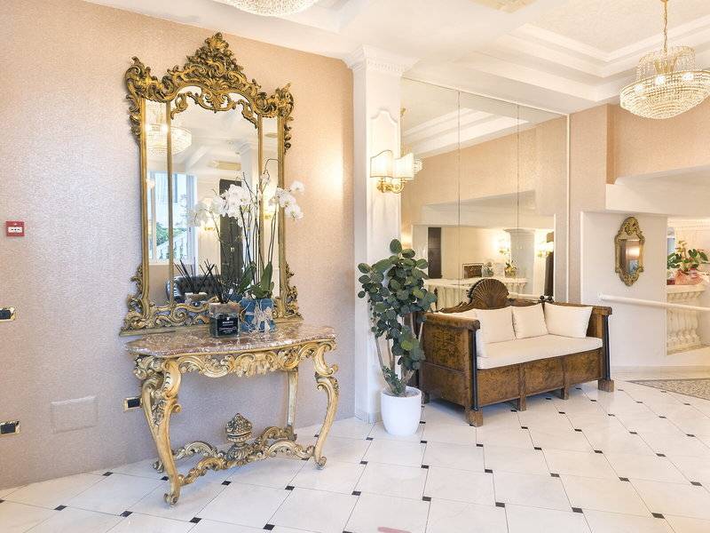 Ein eleganter Eingangsbereich des Baia Imperiale Hotels mit einem goldenen Spiegel, einem Marmortisch, einer Pflanze und einem Sofa.