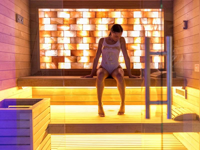 Frau sitzt in einer Sauna des Baia Imperiale Hotels mit einer beleuchteten Wand im Hintergrund.
