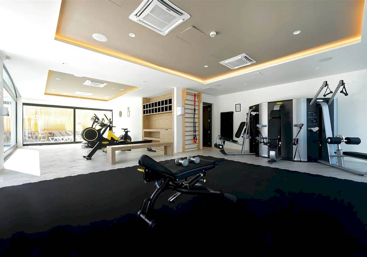 Fitnessbereich im H10 Costa Mogan Hotel mit verschiedenen Trainingsgeräten und einer Glaswand.