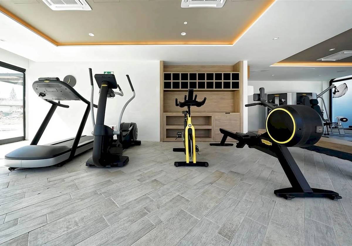 Fitnessbereich im H10 Costa Mogan Hotel mit mehreren Trainingsgeräten und einem Holzschrank.