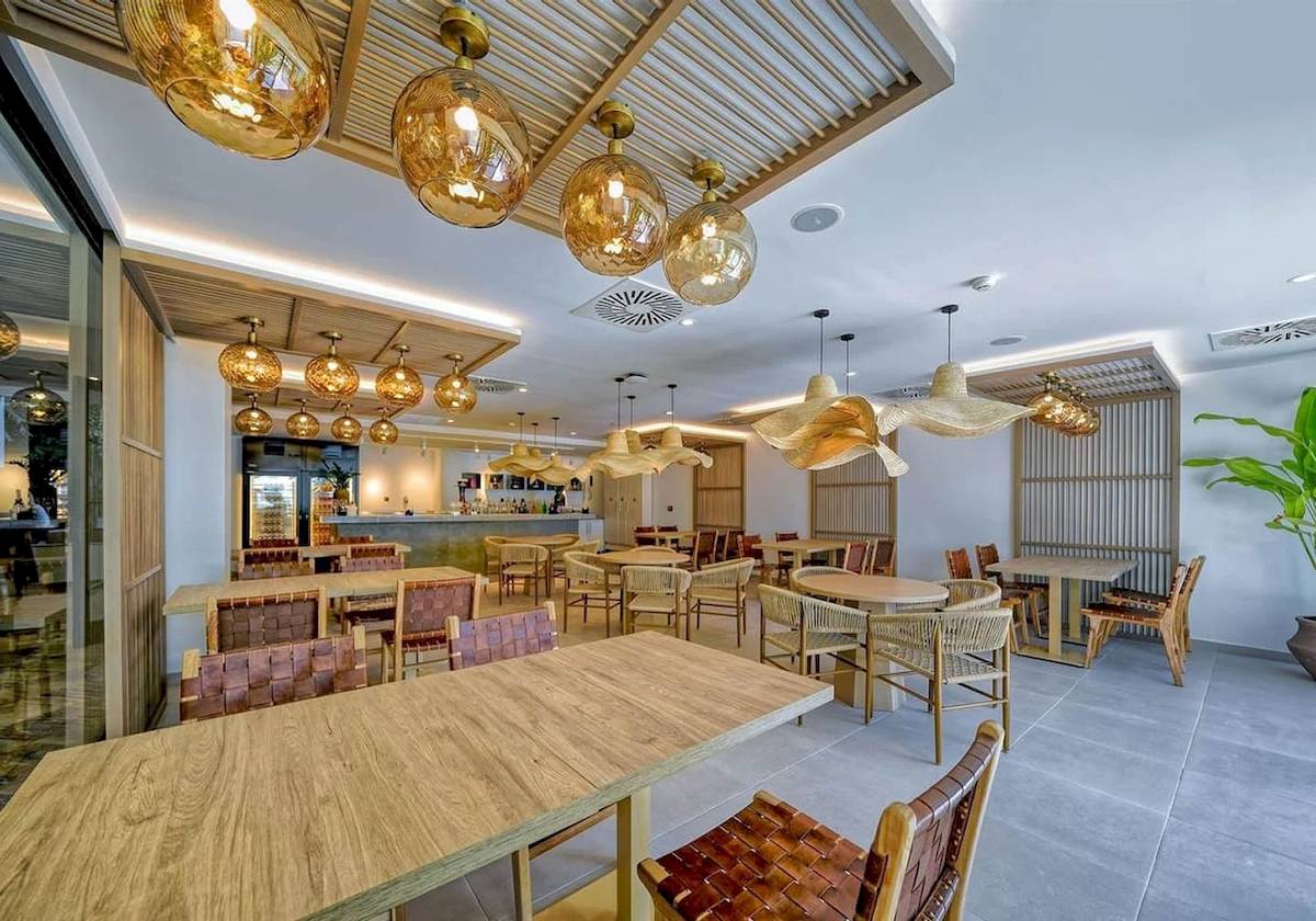 Innenbereich des Restaurants im H10 Costa Mogan Hotel mit modernen Holztischen und Stühlen.