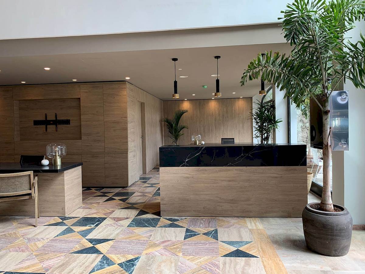 Empfangsbereich des H10 Costa Mogan Hotels mit Marmorboden, Holzmöbeln und Pflanzen.