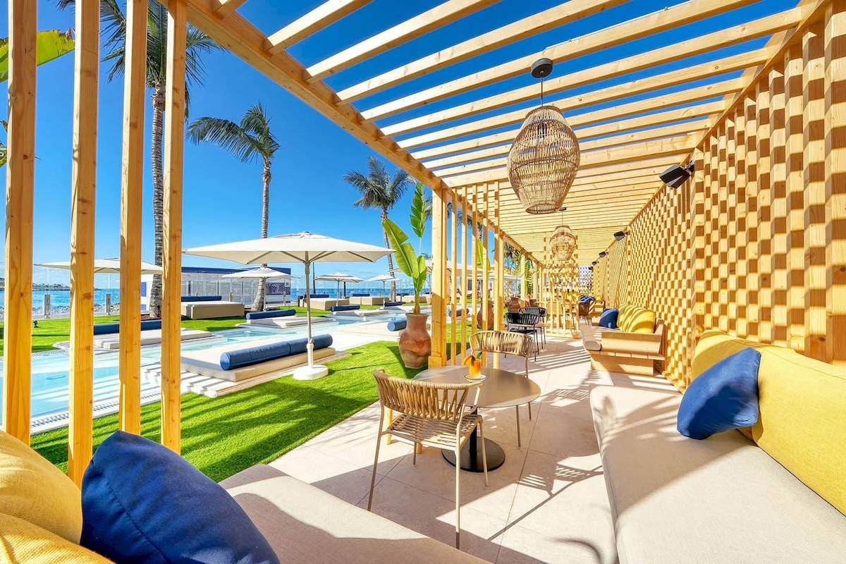 Außenbereich des H10 Costa Mogan Hotels mit Loungebereich, Tischen, Sonnenschirmen und Blick auf den Pool