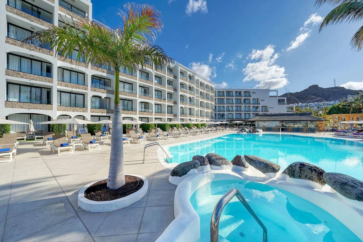 Außenpoolbereich des H10 Costa Mogan Hotels mit Lounge-Liegen und Palme.