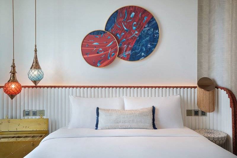Hotelzimmer im W Dubai - Mina Seyahi mit zwei runden Wandgemälden und weißen Bettlaken.