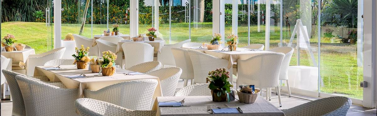 Restaurantterrasse im Acacia Palace Hotel mit weißen Tischen und Stühlen und Blick auf den Rasen
