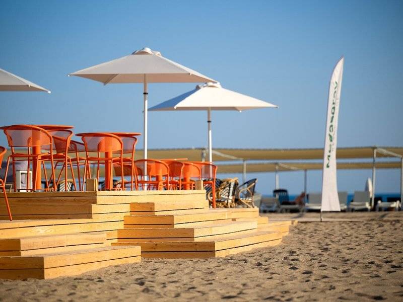 Strandterrasse im Megasaray Resort Side mit orangefarbenen Stühlen und Sonnenschirmen.