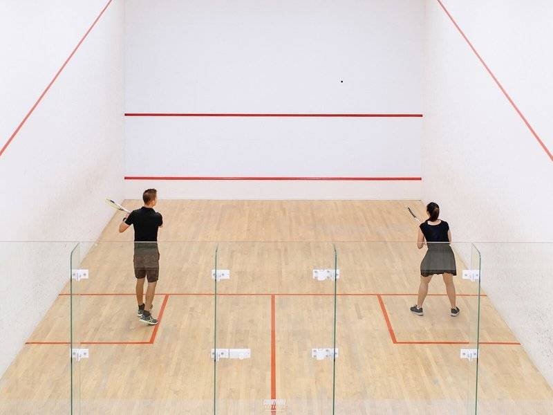 Zwei Spieler auf einem Squashplatz, einer mit Schläger, beide in Aktion.