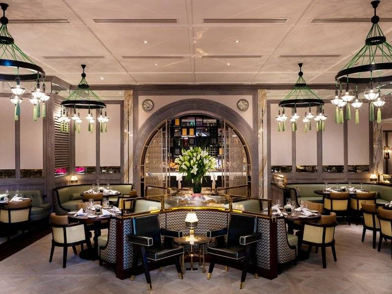 Innenansicht des Restaurants im Sheraton Doha Resort Convention Hotel mit eleganten Möbeln, Tischdecken, Kronleuchtern und einem zentralen Blumenarrangement.