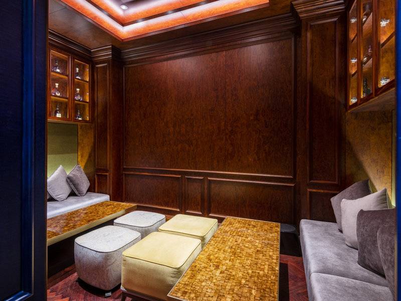 Loungebereich im Sharq Village and Spa, A Ritz Carlton Hotel mit braunen Holzwänden, Sofas und Tischen.