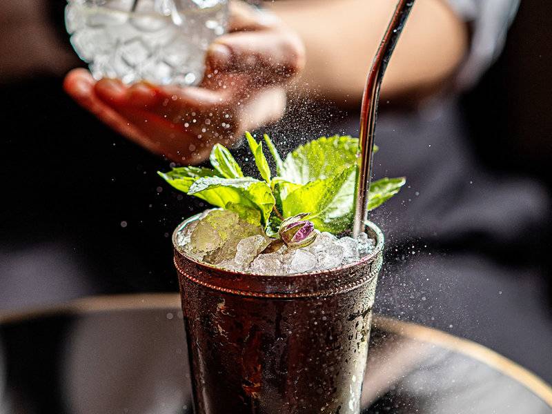 Cocktail mit Minze und Eis in einem Glas, das von einer Person geschüttelt wird.