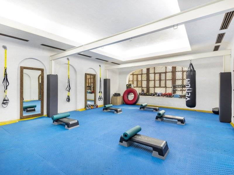 Fitnessraum im Sharq Village and Spa mit blauem Boden und Trainingsgeräten.