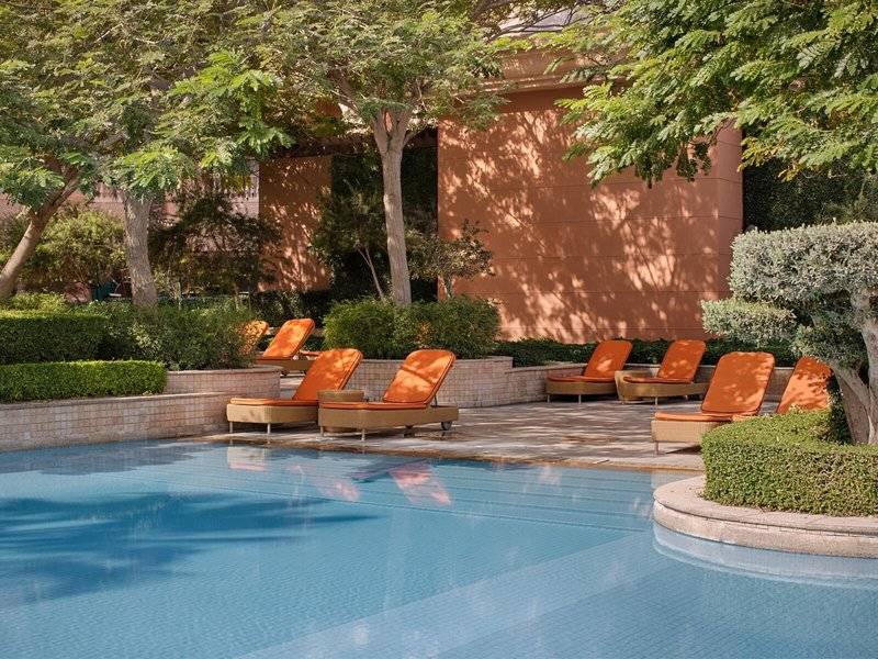 Außenpoolbereich des Marsa Malaz Kempinski mit orange Liegestühlen und Bäumen