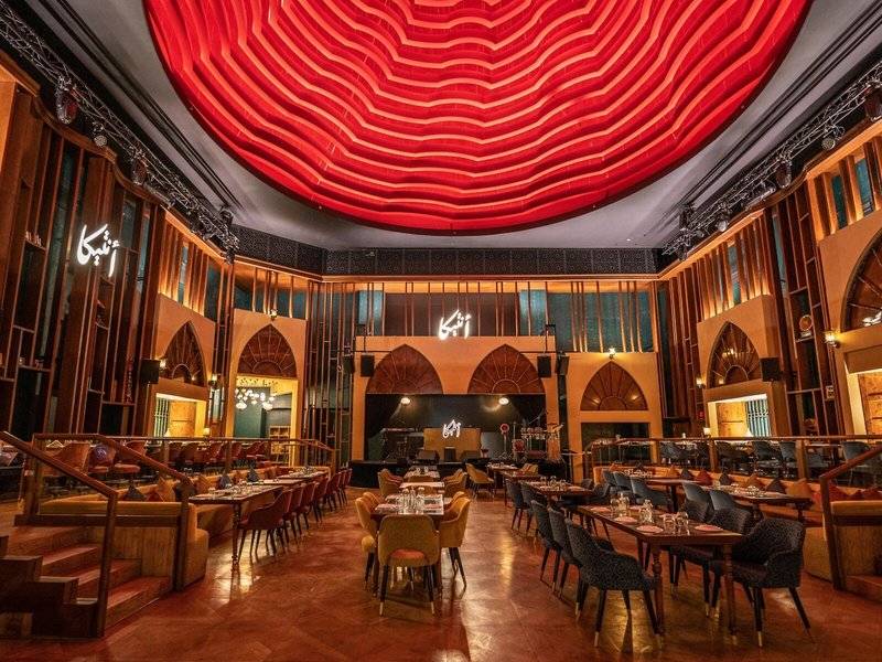 Innenbereich des Marsa Malaz Kempinski, The Pearl mit rotem Deckendesign und vielen Tischen und Stühlen.