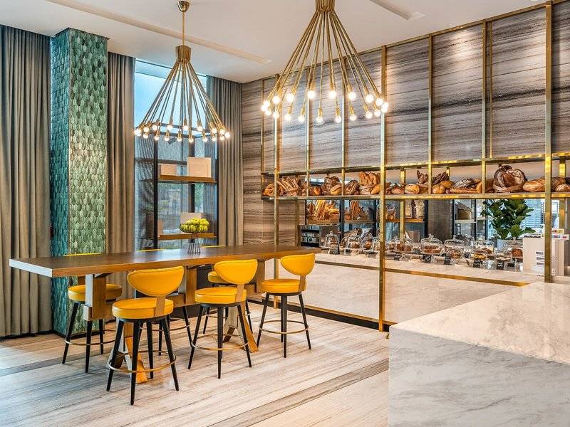 Innenraum des Rixos Gulf Hotel Doha mit gelben Stühlen und einem Esstisch vor einer goldenen Wand mit Bäckereiprodukten.