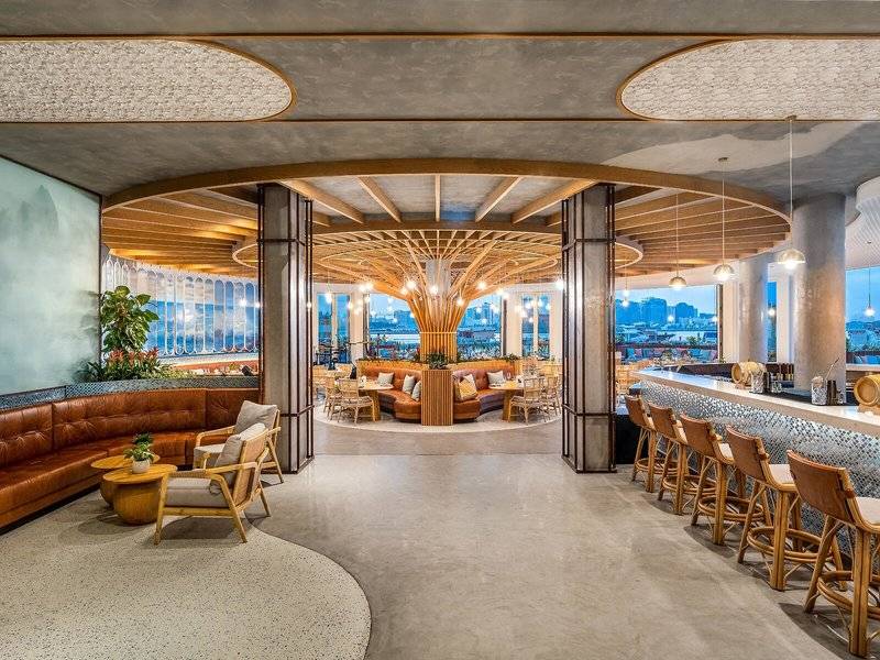 Innenansicht der Lounge im Rixos Gulf Hotel Doha mit Holzmöbeln und Panoramafenstern.