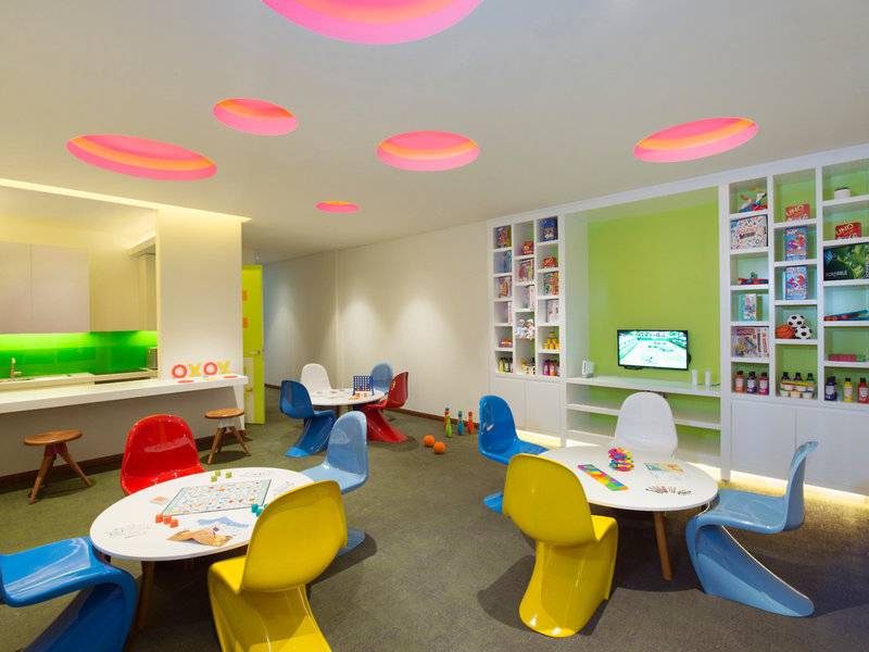 Spielzimmer im Banana Island Resort Doha by Anantara mit bunten Stühlen, Tischen und rosa Kreisen an der Decke.