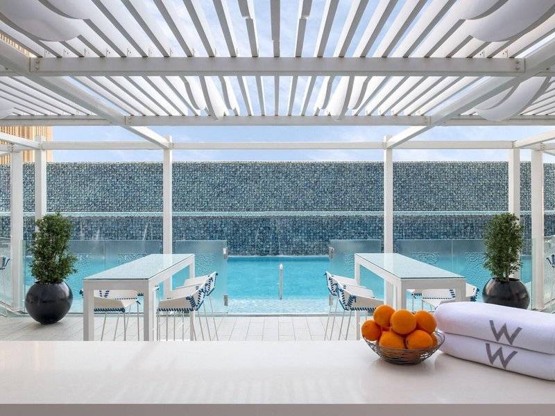 Pool im W Doha Hotel & Residences mit blauen Stühlen und Wasserfall.