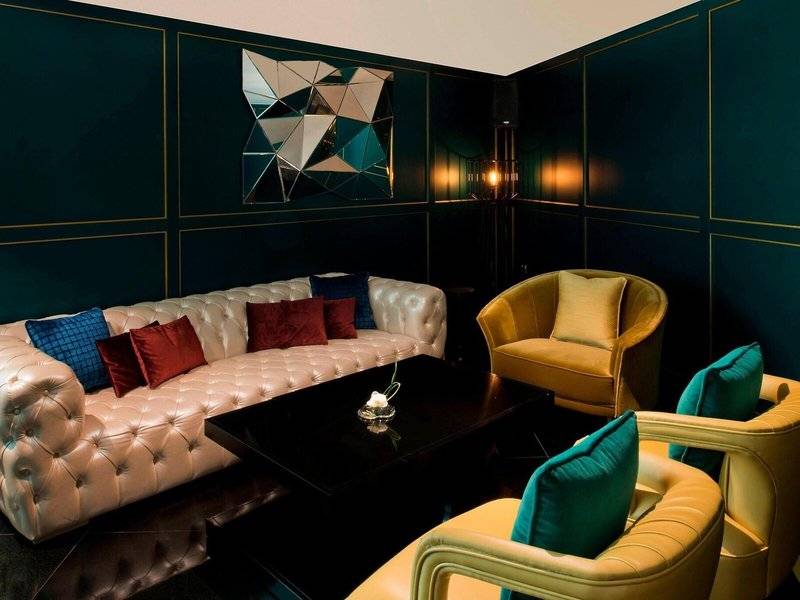 Loungebereich im W Doha Hotel & Residences mit dunkelgrünen Wänden, weißen Möbeln und gepolsterten Sesseln.