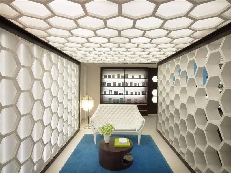 Inneneinrichtung des W Doha Hotel & Residences mit weißen Hexagon-Wänden, einem weißen Sofa, einem runden Tisch und einer Lampe.