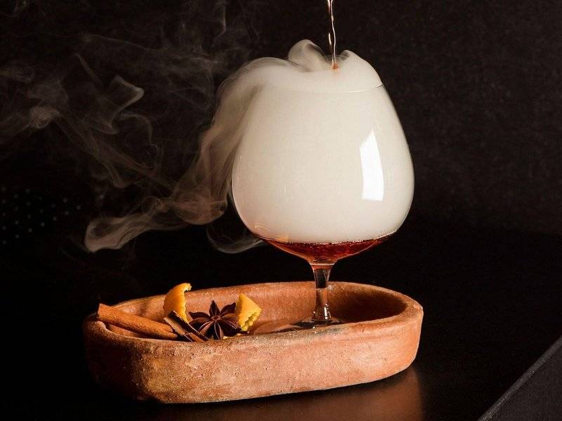 Cocktail mit Raucheffekt im Glas, serviert auf einem Tablett mit Gewürzen.