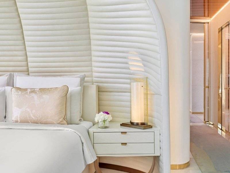Schlafzimmer im Fairmont Doha Hotel mit weißen Möbeln, einem Bett, Kissen und einer Lampe auf dem Nachttisch.