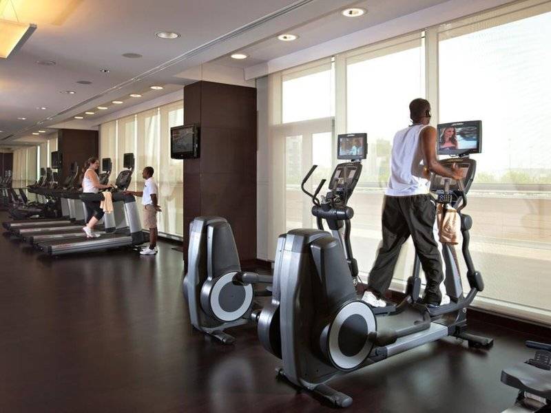 Fitnesscenter im Hyatt Regency Oryx Doha mit Läufern auf Geräten und Fernsehern