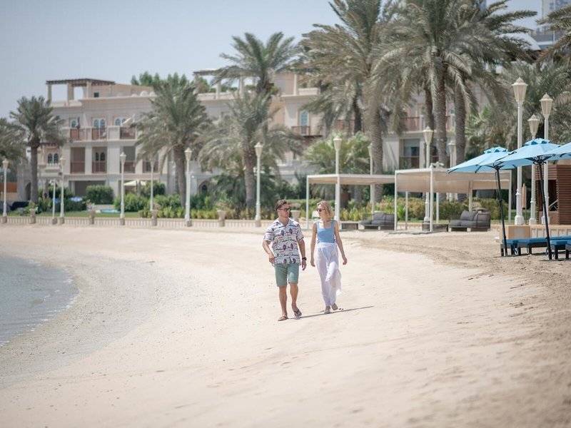 Paar am Strand vor dem Four Seasons Hotel Doha, Gebäude im Hintergrund, Palmen und Sonnenschirme