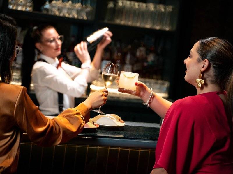 Vier Frauen an einer Bar im Four Seasons Hotel Doha, eine bedient die Gäste, während die anderen einen Drink genießen.