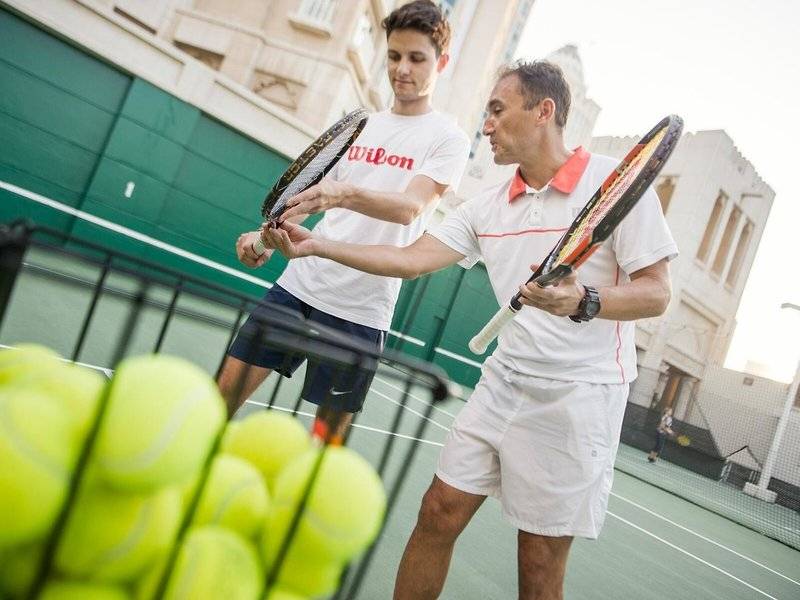 Zwei Männer auf dem Tennisplatz im Four Seasons Hotel Doha, einer hält eine Tennisschläger und der andere hält einen Ball.