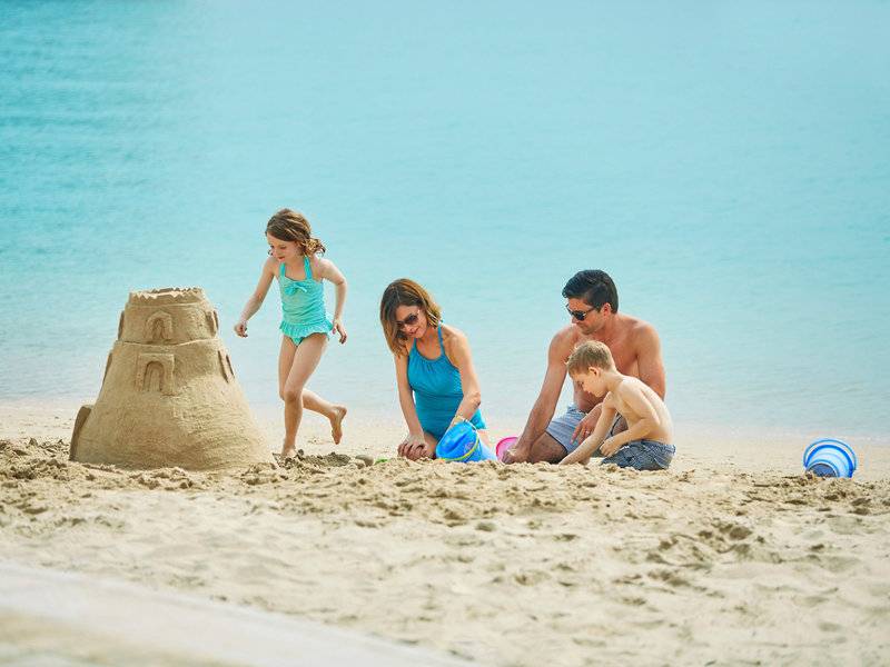 Eine Familie baut eine Sandburg am Strand, während das Meer im Hintergrund ist.