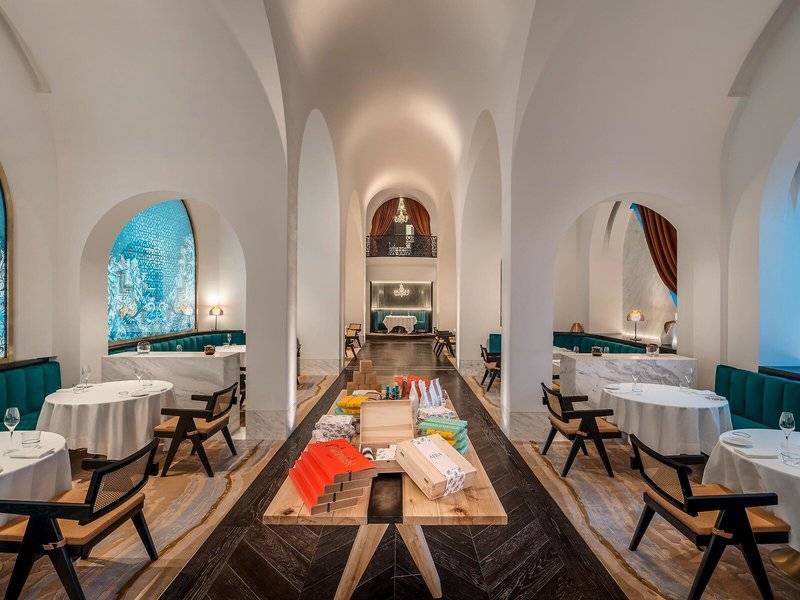Innenansicht des Restaurants im Raffles Doha mit runden Tischen, Bänken und dekorativen Elementen.