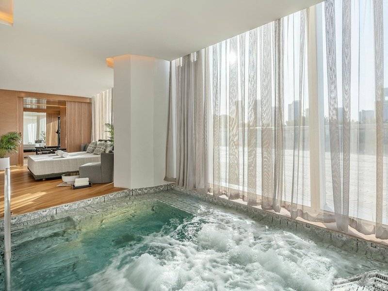 Ein eleganter Innenpool im Raffles Doha Hotel mit fließendem Wasser und einer Stadtansicht durch große Fenster.