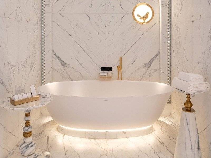 Badezimmer im Raffles Doha mit einer weißen Badewanne, Marmorwänden und goldenen Armaturen.