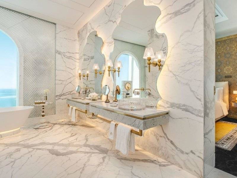 Luxuriöses Badezimmer im Raffles Doha mit Marmorwänden, Doppelwaschbecken und großen Spiegeln.