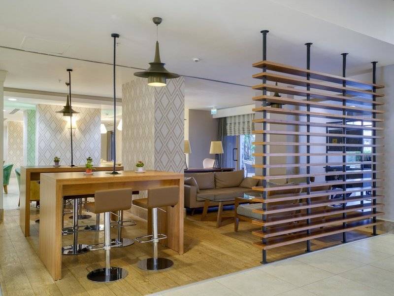 Innenbereich des Grand Park Lara Hotels mit Holzmöbeln, Barhockern, Couch und geometrischer Wandgestaltung.