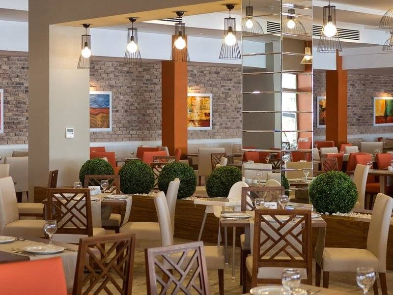 Innenansicht des Grand Park Lara Restaurants mit gedeckten Tischen, Sitzgruppen und dekorativen Pflanzen.