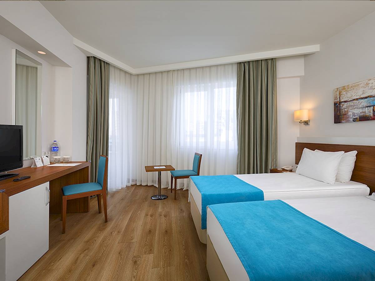 Innenansicht eines Doppelzimmers im Grand Park Lara Hotel mit zwei Betten, Schreibtisch und Fernseher.