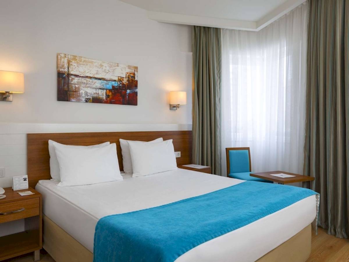 Schlafzimmer im Grand Park Lara Hotel mit einem Doppelbett, zwei weißen Kissen, blauer Decke, und einem blauen Stuhl neben einem Tisch.