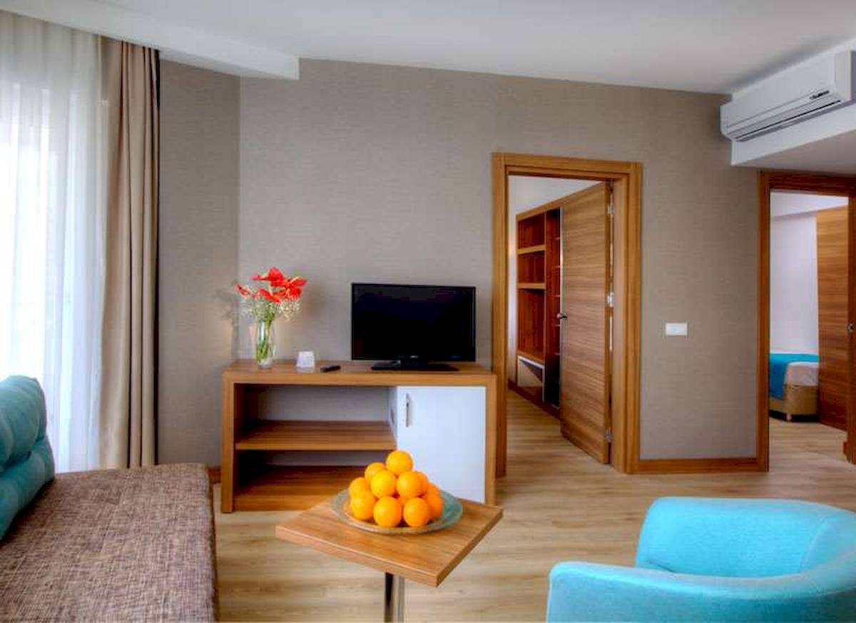 Innenansicht eines Hotelzimmers im Grand Park Lara mit Fernseher, Tisch, Obst und Türen.