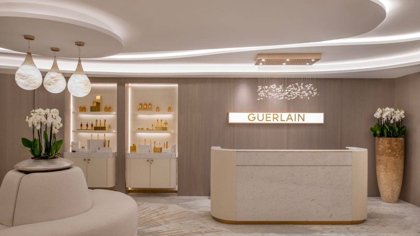 Innenansicht der Guerlain Boutique im St. Regis Doha mit weißem Empfangstresen, Marmorboden und Beleuchtung.